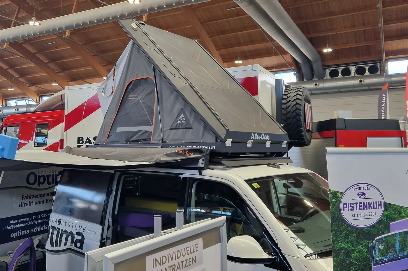 Alu-Cab Aluminium-Keilzelt aufgeklappt auf einem weissen VW Bus mit Dachplattform in der Messehalle
