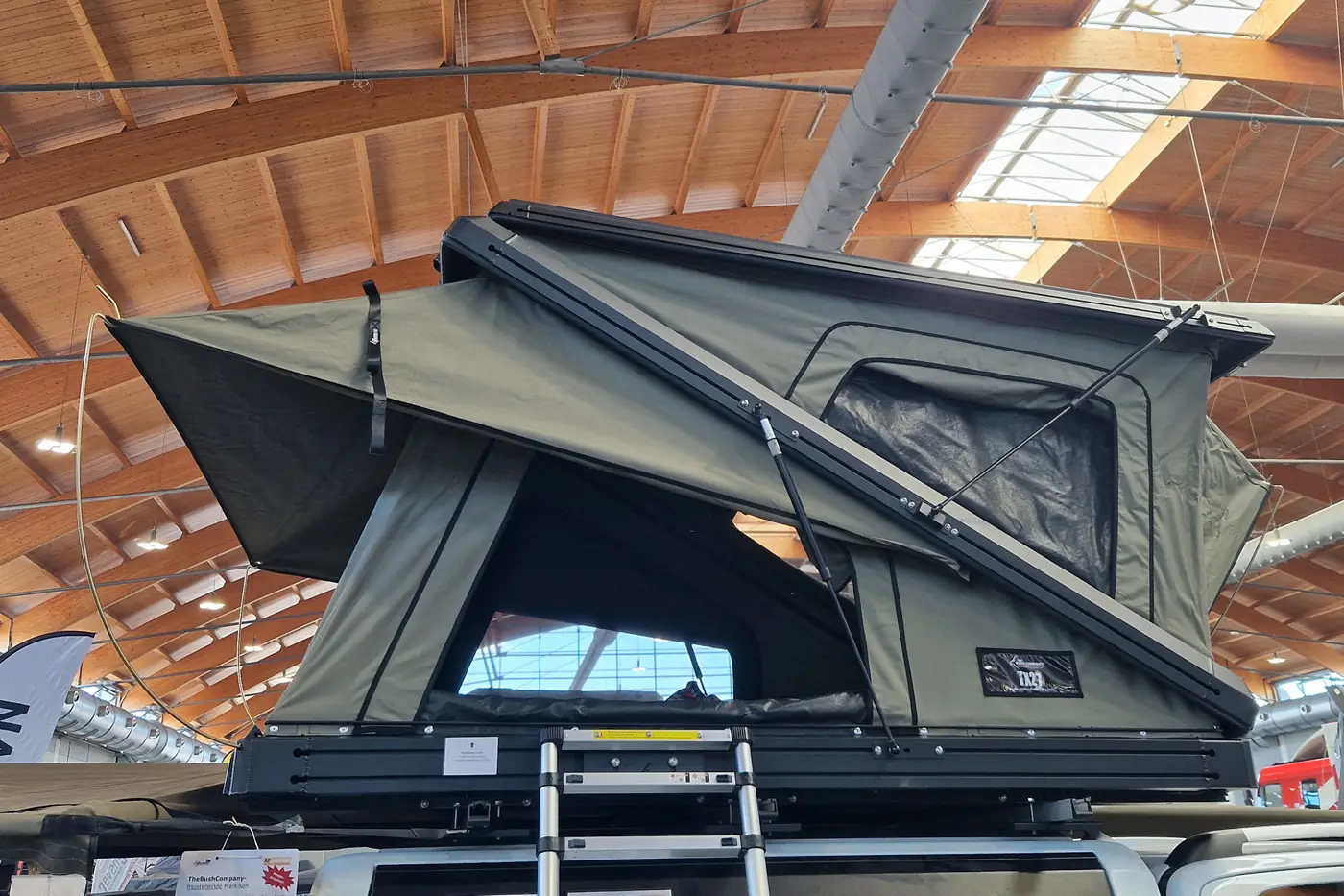 Gruenes Hartschalen-Keilzelt mit grossen Panoramafenstern, aufgebaut auf einem Pickup mit Leiter