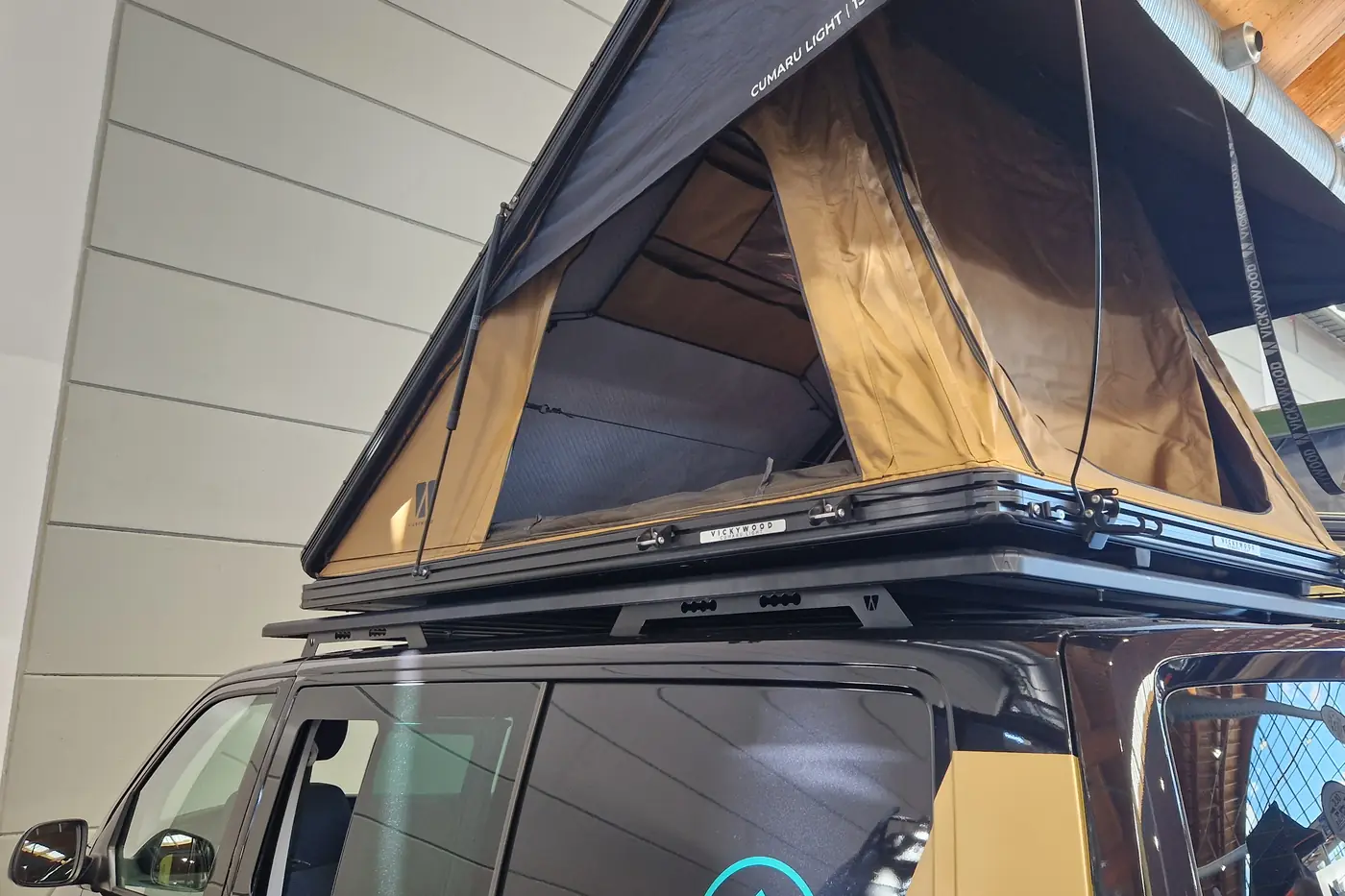 Keilzelt mit dunkler Hartschale und beigem Zeltstoff auf einem VW Bus mit flachem Plattformtraeger